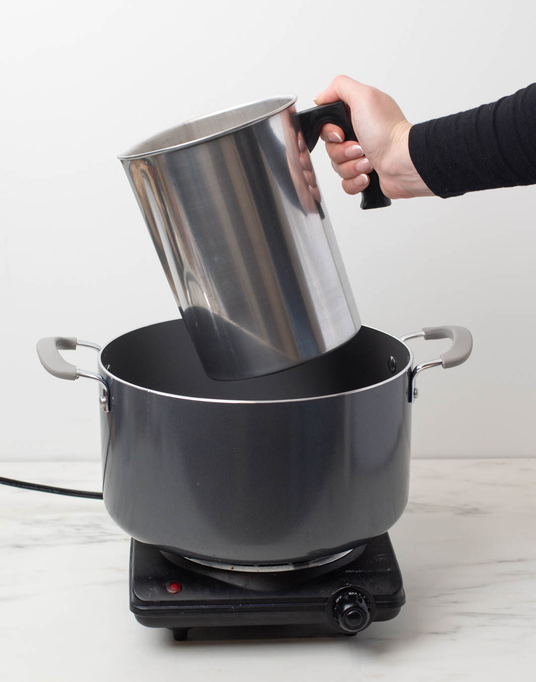 A hand placing a pouring pitcher into a pot on a double boiler.